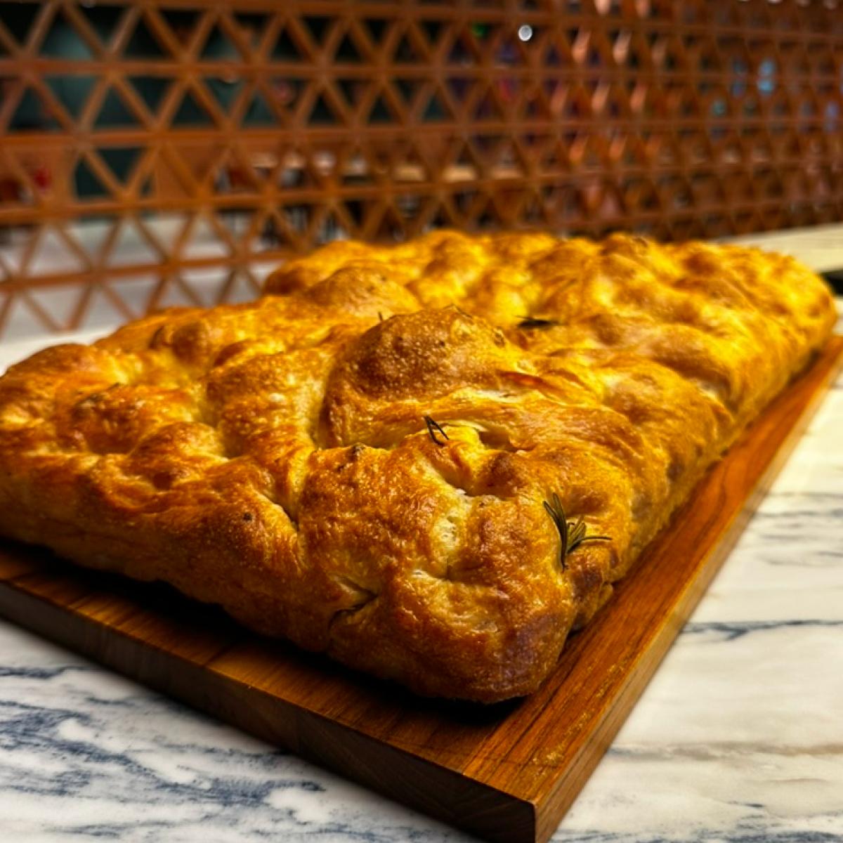 Focaccia dourada inteira sobre tábua de madeira
